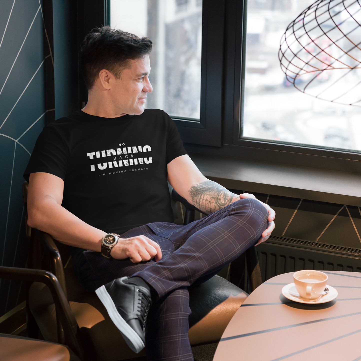 Man wearing comfortable men's fashion t-shirt sitting by window with coffee cup at table