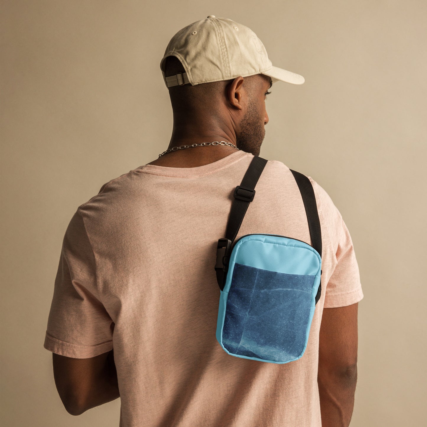 PJ Designs unisex streetwear bag in blue worn crossbody by man in beige cap and pink shirt