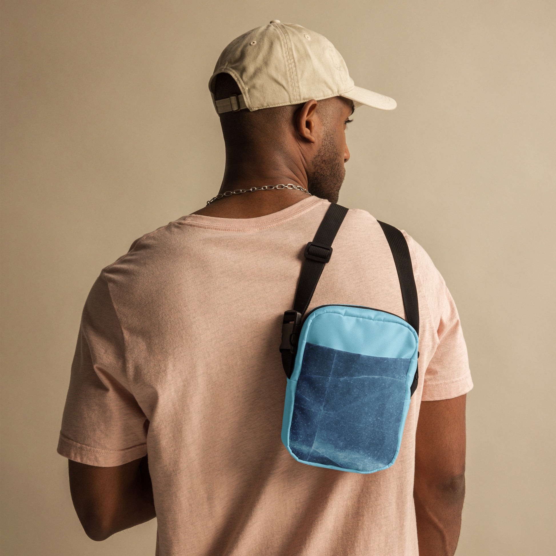 PJ Designs unisex streetwear bag in blue worn crossbody by man in beige cap and pink shirt